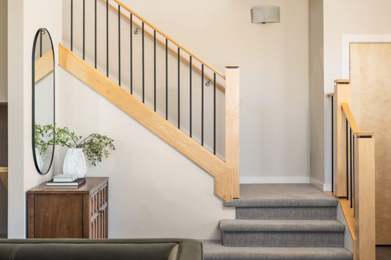 Carpeted staircase with an oak handrail and black balusters above a mirror and console