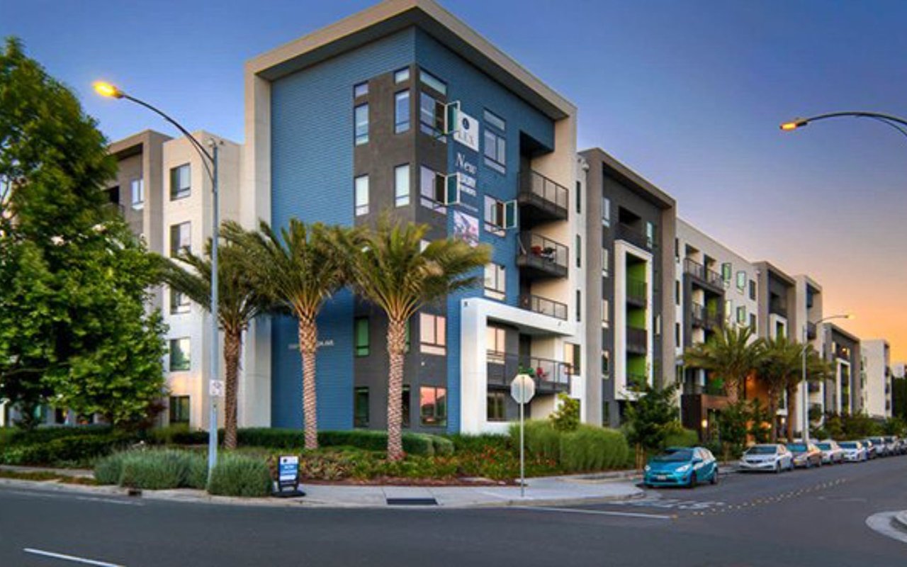 Modern apartment building with blue facade, balconies, and palm trees at dusk.