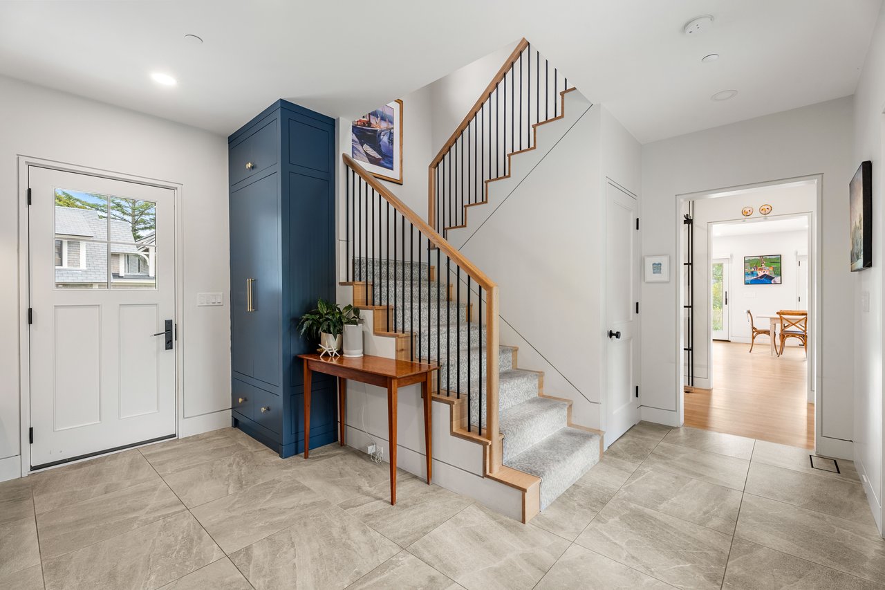 Bright entryway with a navy built-in cabinet, tiled floor, and wood-trimmed staircase with black railings.