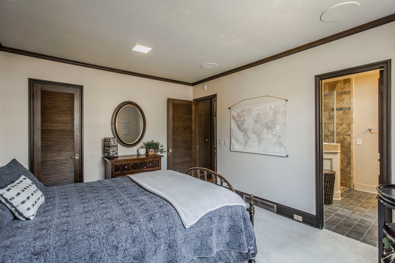 Bedroom with a blue-gray quilted bed, dark wood trim, and an open doorway to a tiled bathroom.