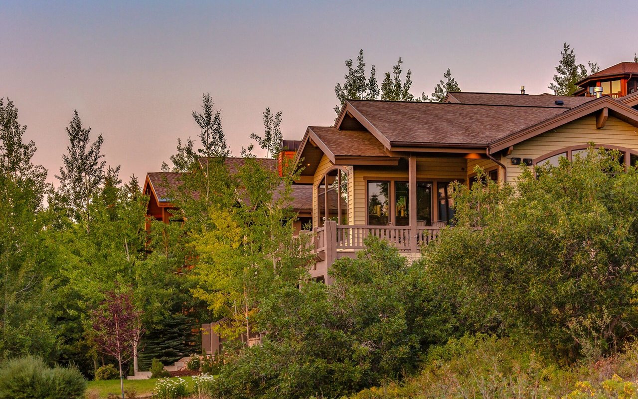 Wood-sided home with a raised deck surrounded by trees and greenery.