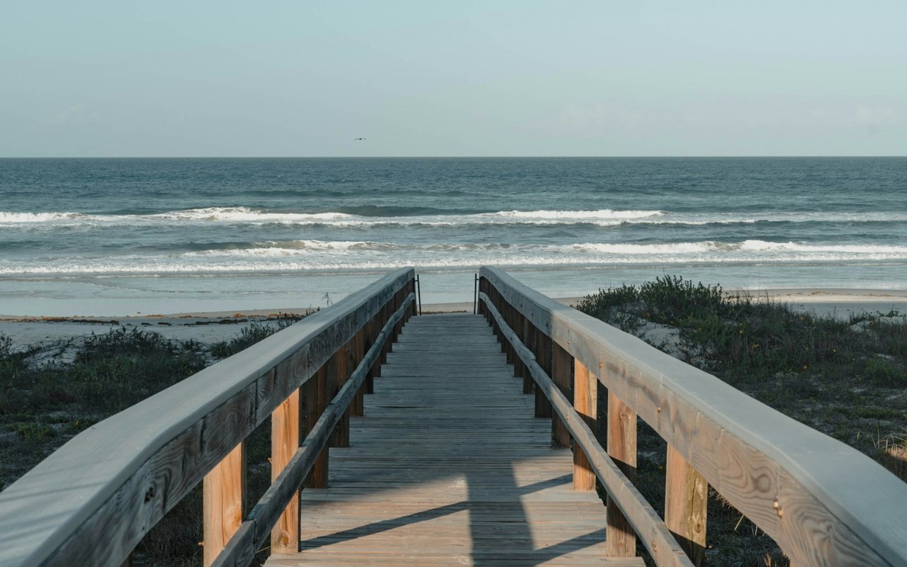 A wooden boardwalk leads across coastal plants and sand to the ocean in Indialantic.