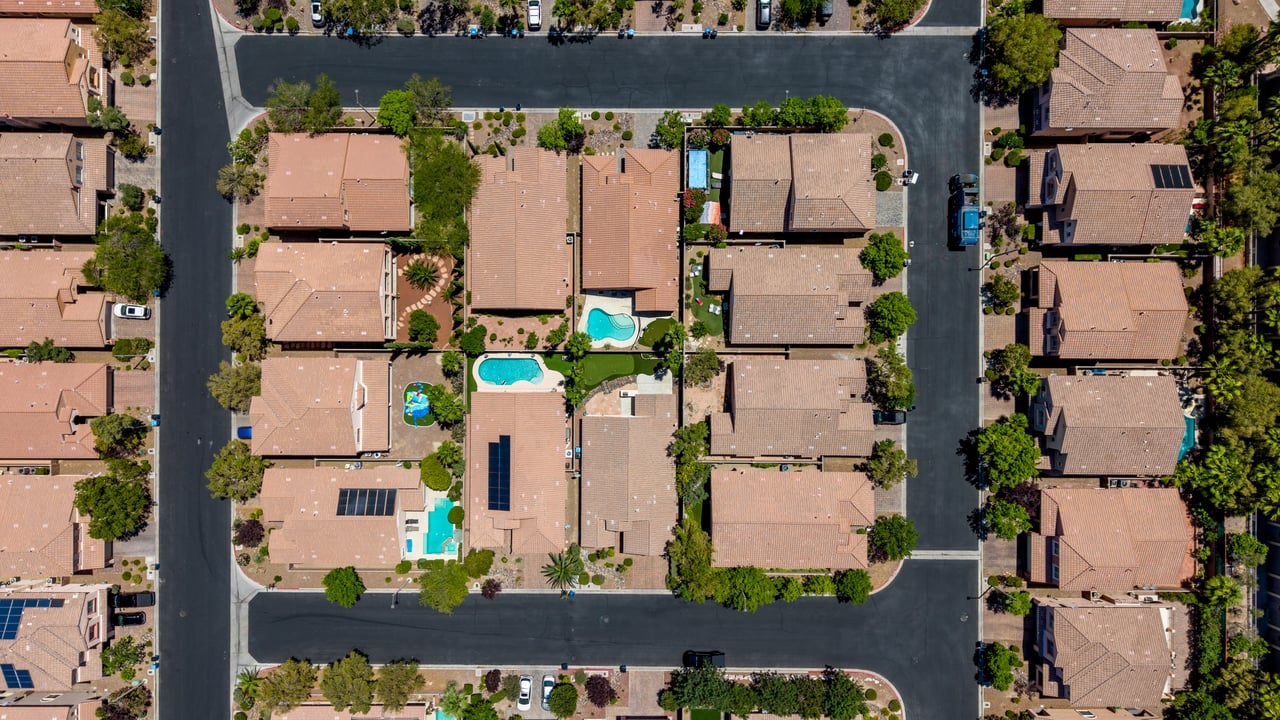 Aerial view of a residential block with tile-roof homes, landscaped yards, and swimming pools.