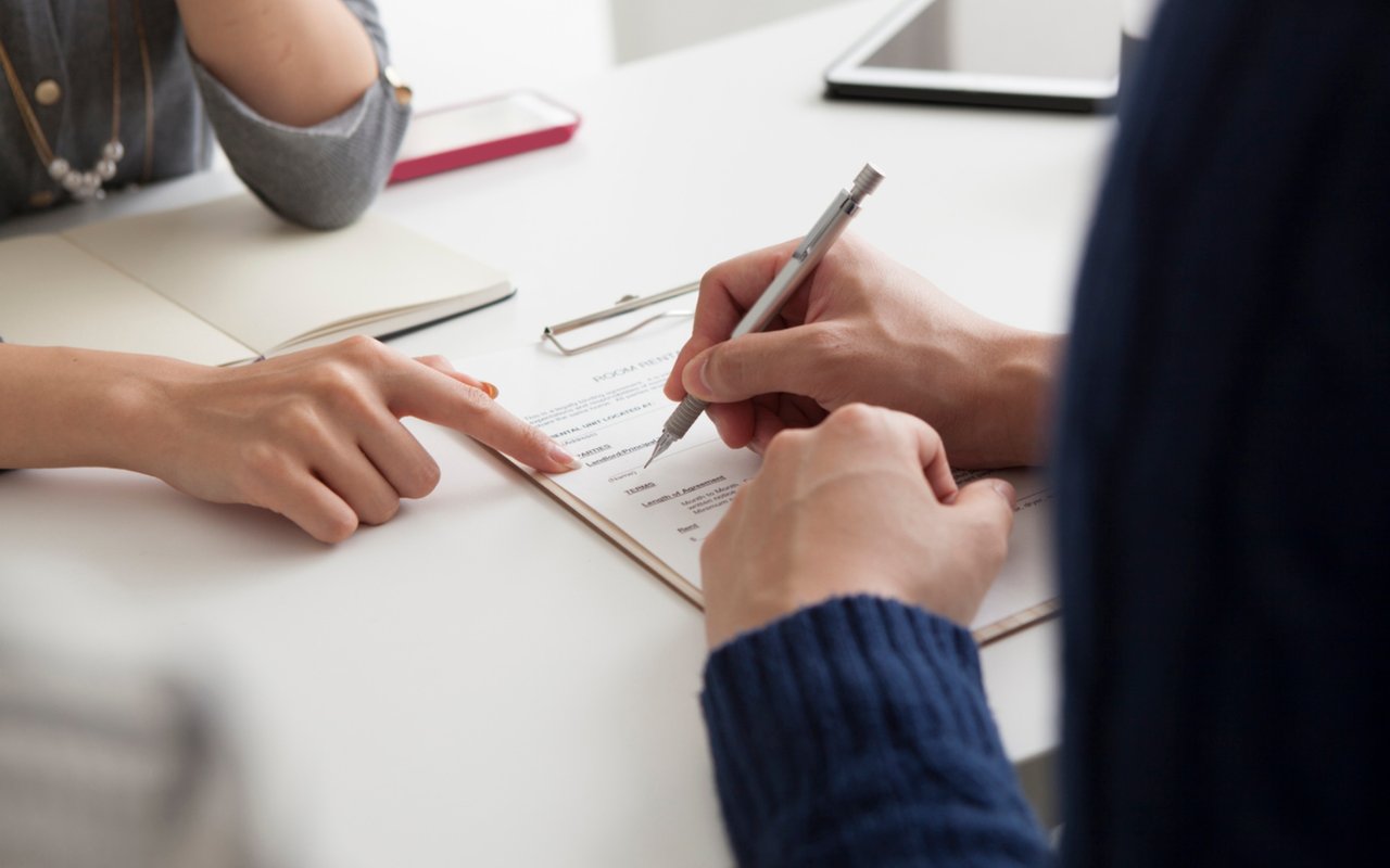 Two people review a document as one points to a line and the other signs.