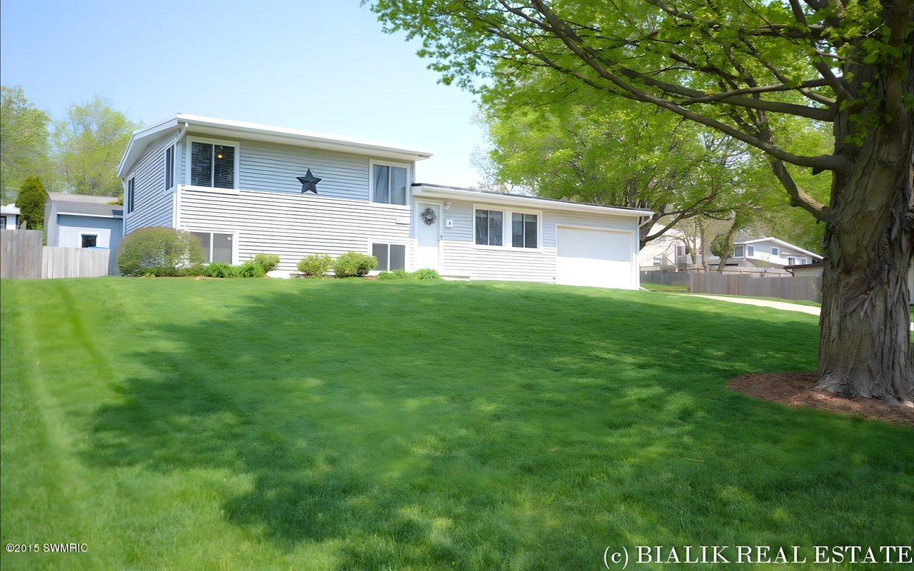 White split-level home with a broad green lawn and a large shade tree.