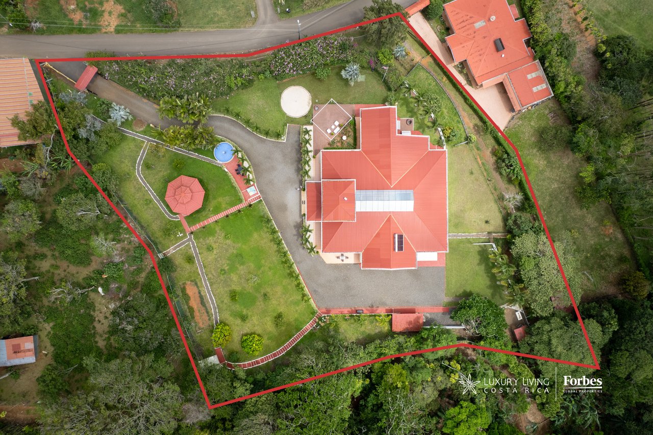 Aerial view of a red-roofed house, landscaped grounds, small pool, and gazebo within a red property boundary.
