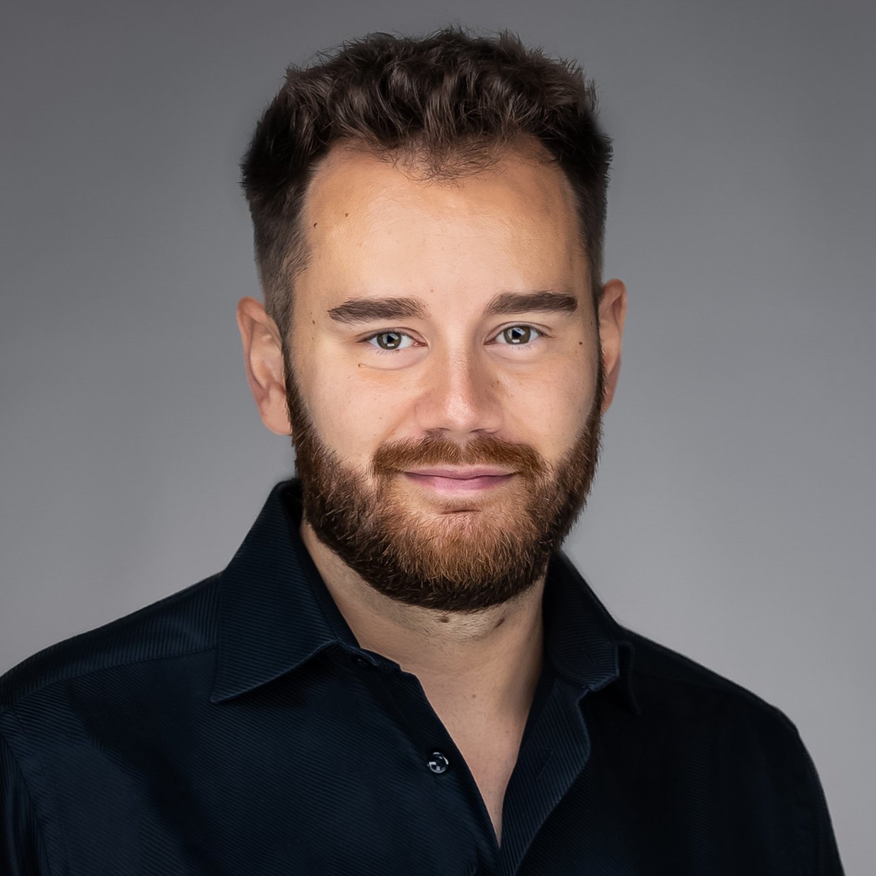 Daniel Mocanu, wearing a dark collared shirt against a gray background.