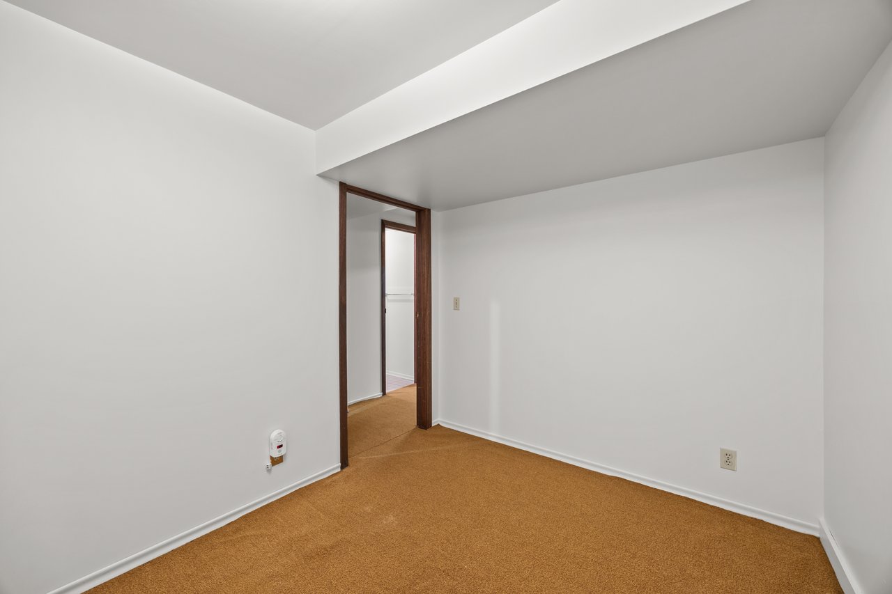 Empty room with golden-brown carpet, white walls, and a dark wood-trimmed doorway.