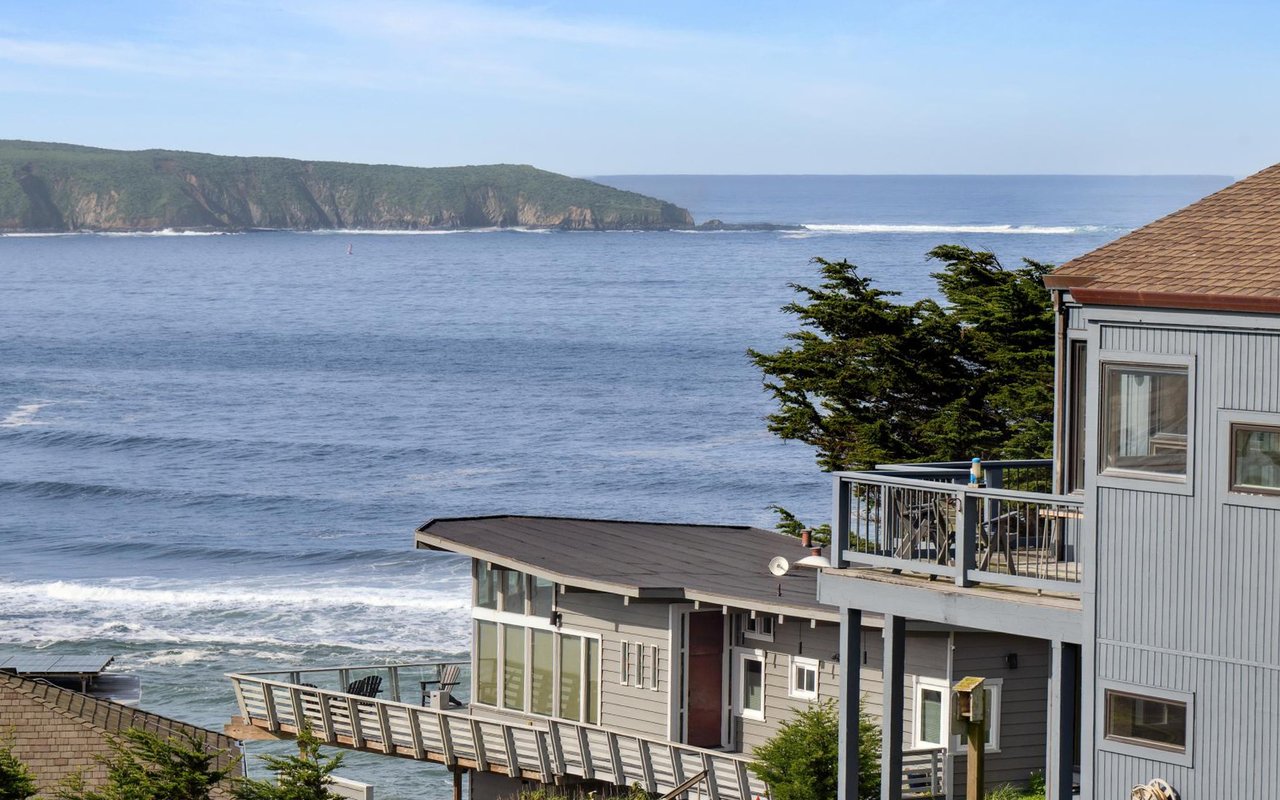 Coastal homes overlook the ocean, with broad decks and a rugged green headland.
