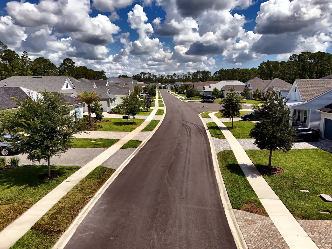 Elevated view of a Palm Crest street with sidewalks, young oaks and coastal-style homes under a sky of white clouds.