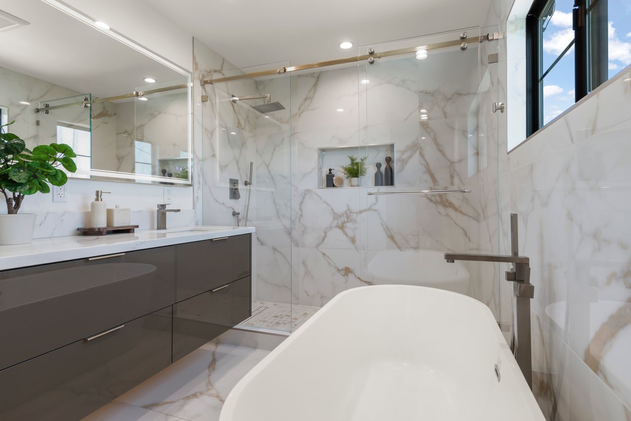 Bathroom with a freestanding soaking tub, glass shower, dark vanity, and marble-patterned tile.