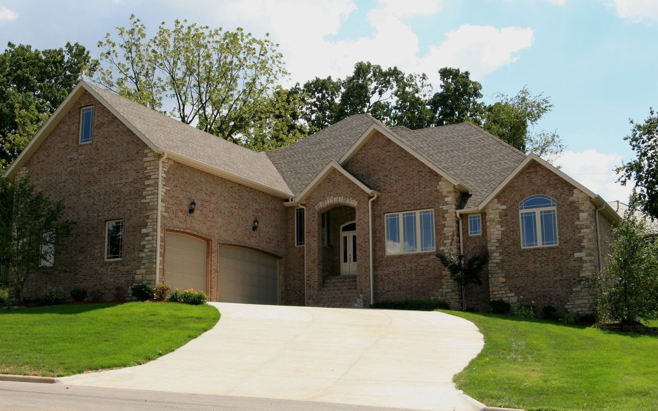 Brick-and-stone house with multiple gables and a wide curved driveway leading to two garage doors.