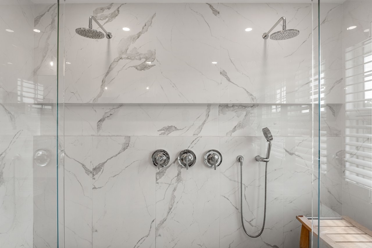 Walk-in shower with veined marble-look tile, dual rainfall showerheads, and a handheld sprayer.