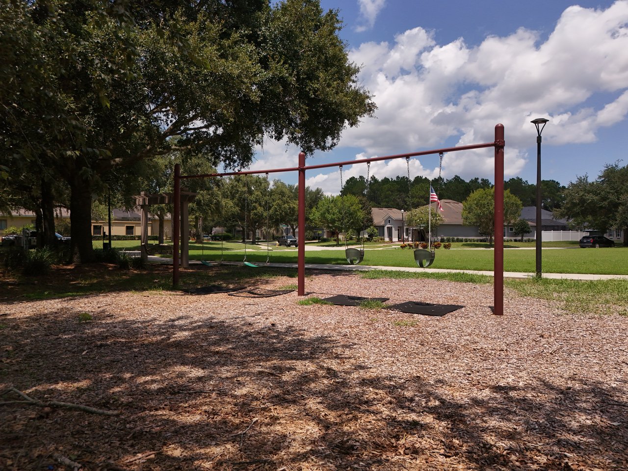 Community playground with swings beneath large trees, with Austin Park homes in the background.