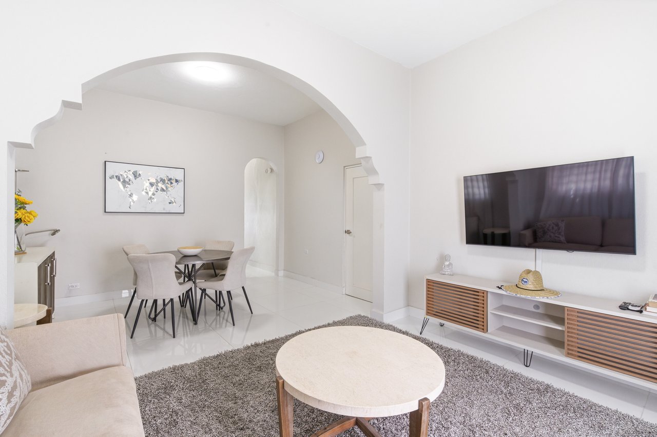 Living and dining area with a broad archway, wall-mounted television, and round coffee table.