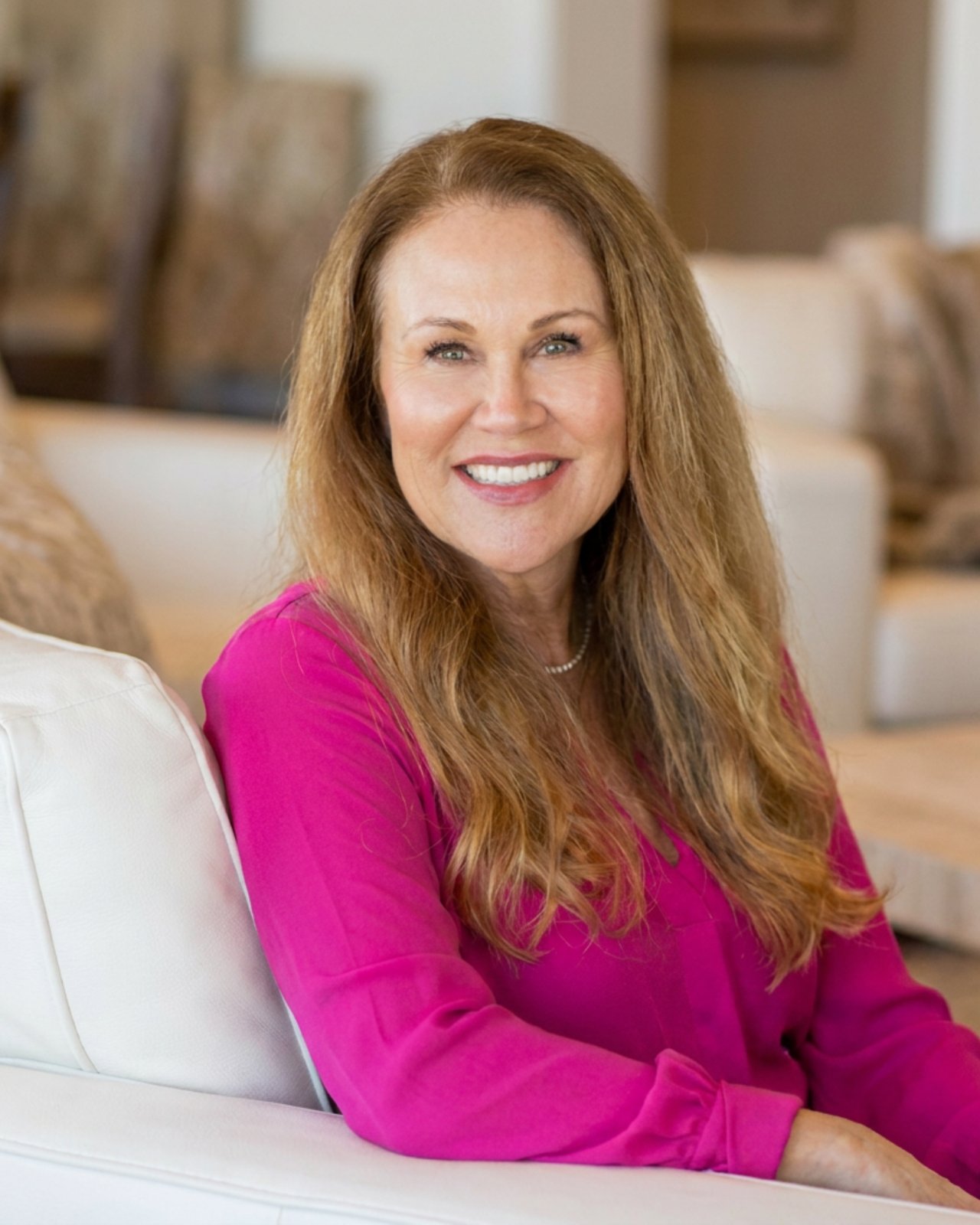 Kristan Lynch Ayala seated in a white chair, smiling in a bright pink blouse.