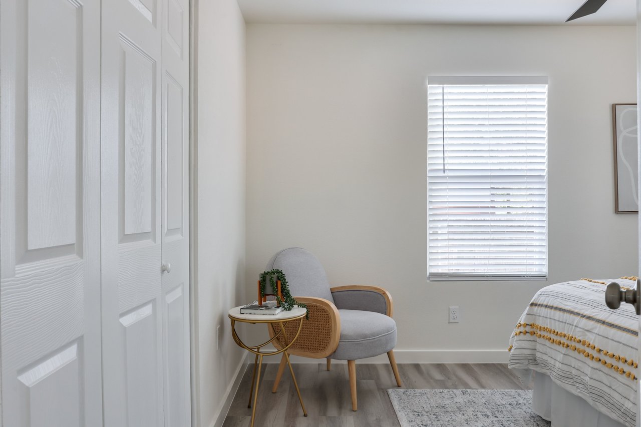 Bedroom with white closet doors, a gray accent chair, and a bed beside a window with blinds.
