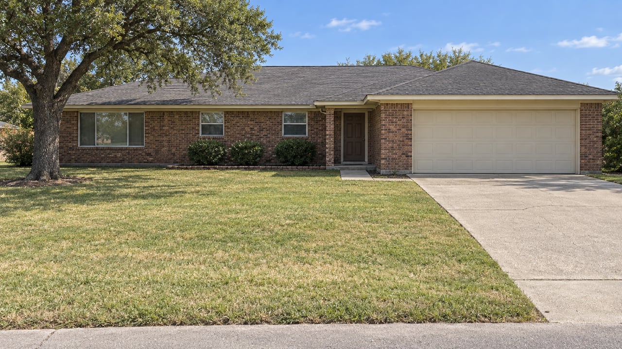 Red-brown brick ranch behind a deep, partly straw-colored lawn, with a mature bur oak and a concrete driveway.