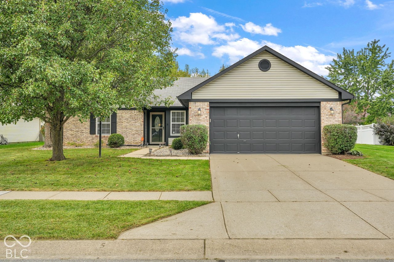 Single-story brick home with a dark double garage and a large front-yard tree.