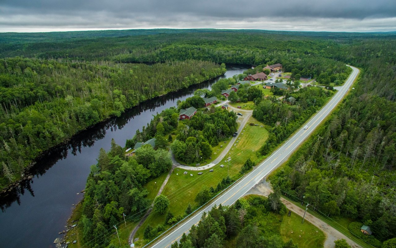 Aerial view of a wooded riverside community with scattered homes and a highway.
