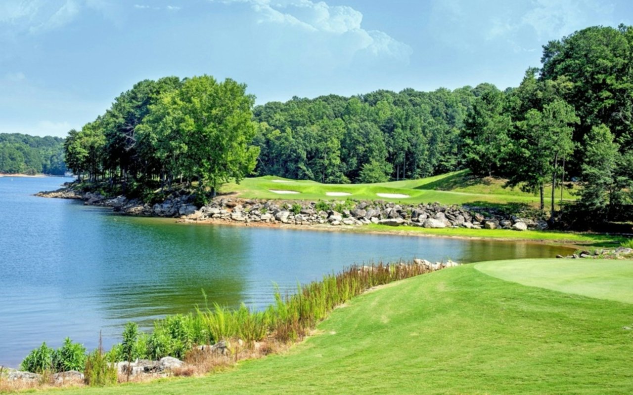 Lakeside golf course with green fairways, rocky shoreline, and wooded hills.