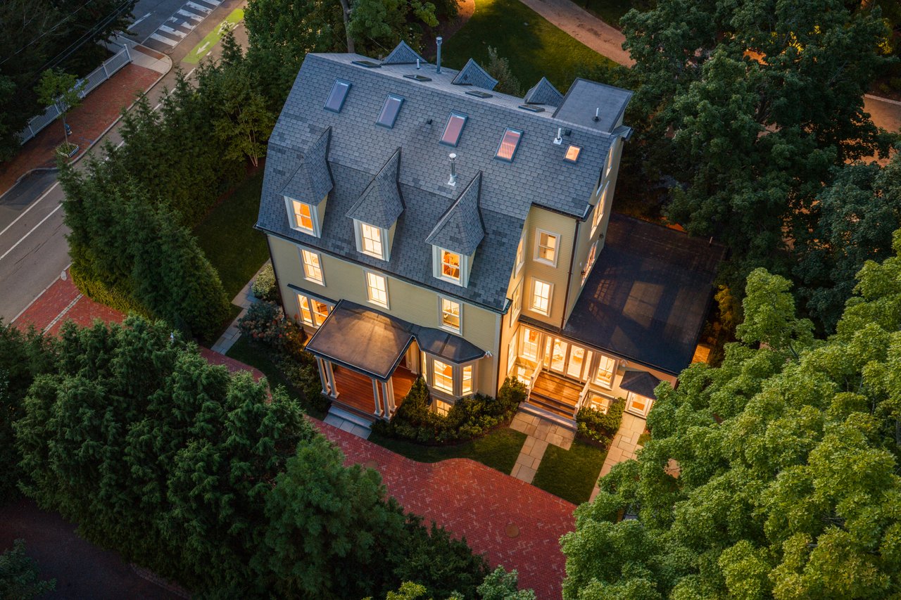 Aerial view of a Victorian house at dusk, with a slate roof, glowing windows, and a curved brick walkway.