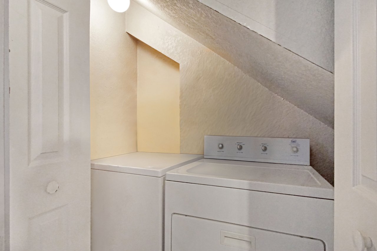 Laundry area at 2506 Nugget Lane in Tallahassee, Florida, with a white top-loading washing machine and dryer set beneath an angled ceiling. The appliances are tucked into a closet with bifold doors and overhead lighting.