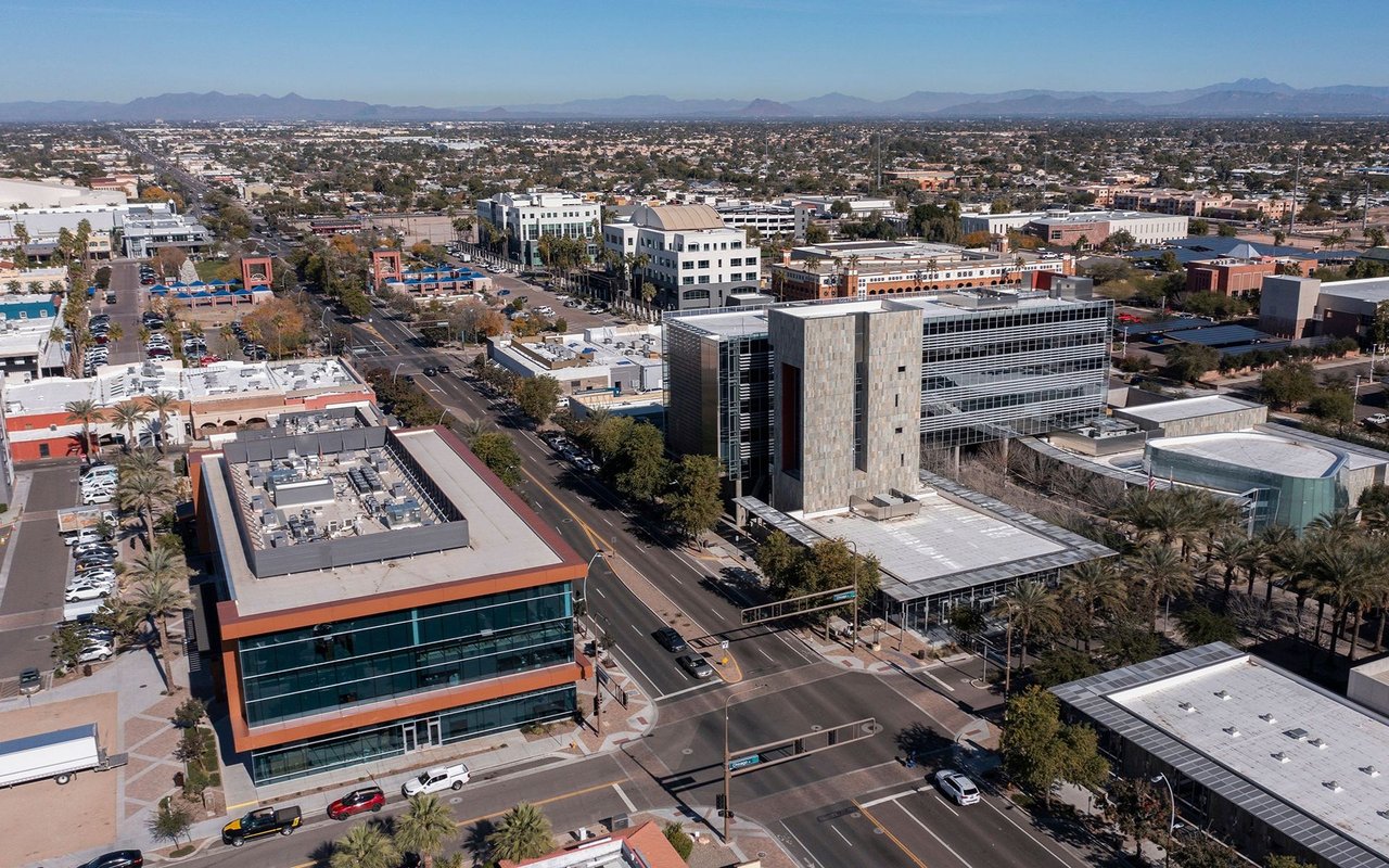 Aerial view of an urban district with modern commercial buildings, palm-lined streets, and distant mountains.