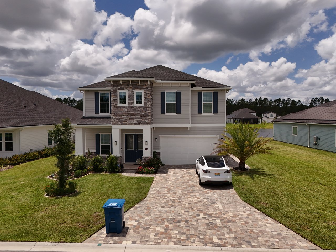 Two-story home with stone facade accents, a paver driveway, and a white car parked in front.
