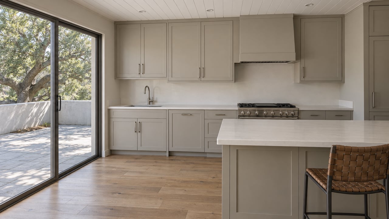 Renovated kitchen with an oak island, gray cabinetry, and a glazed slider overlooking a paved terrace and oak tree.