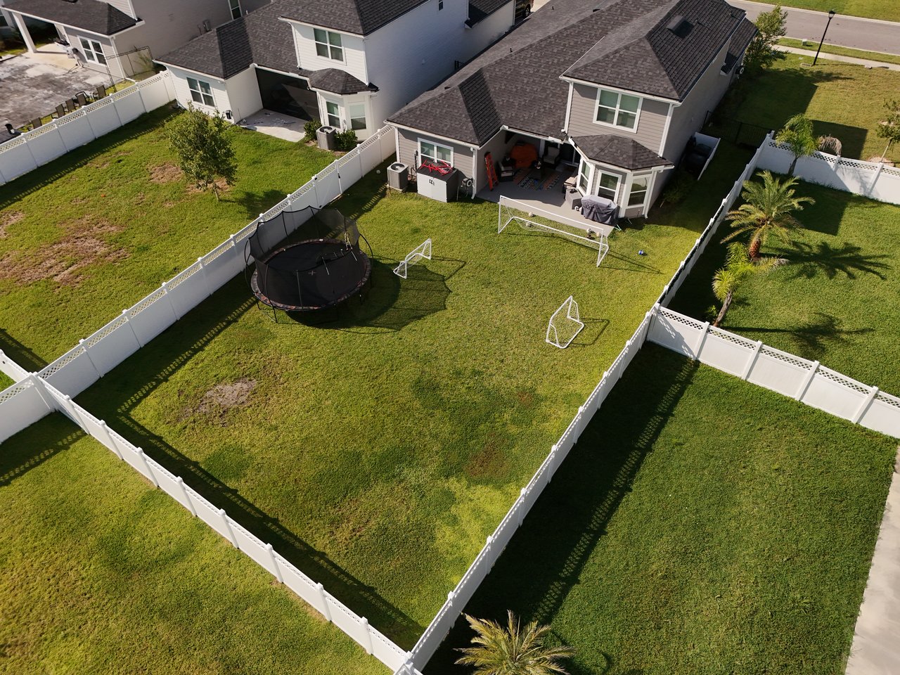 Aerial view of a fenced backyard with a trampoline, soccer goals, and covered patio.