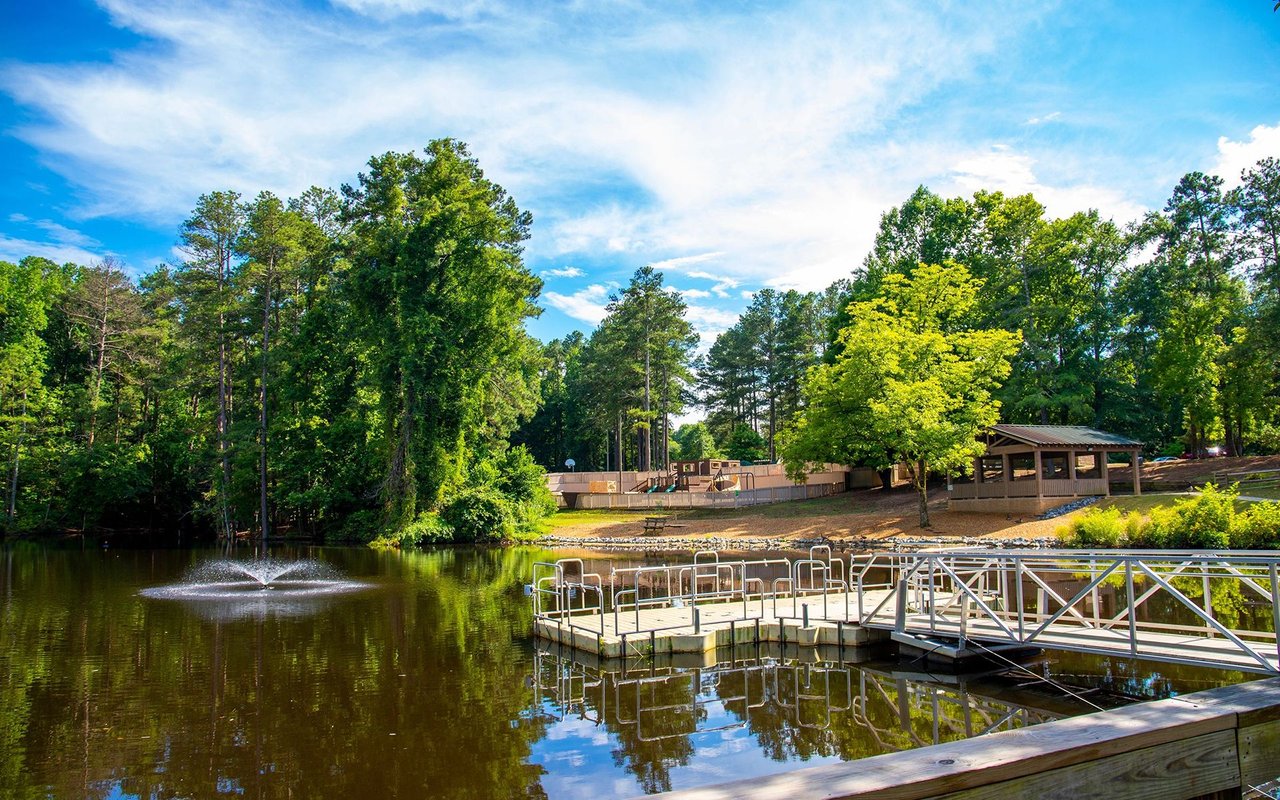 Woodstock park pond with a floating dock, fountain, and wooded shoreline.