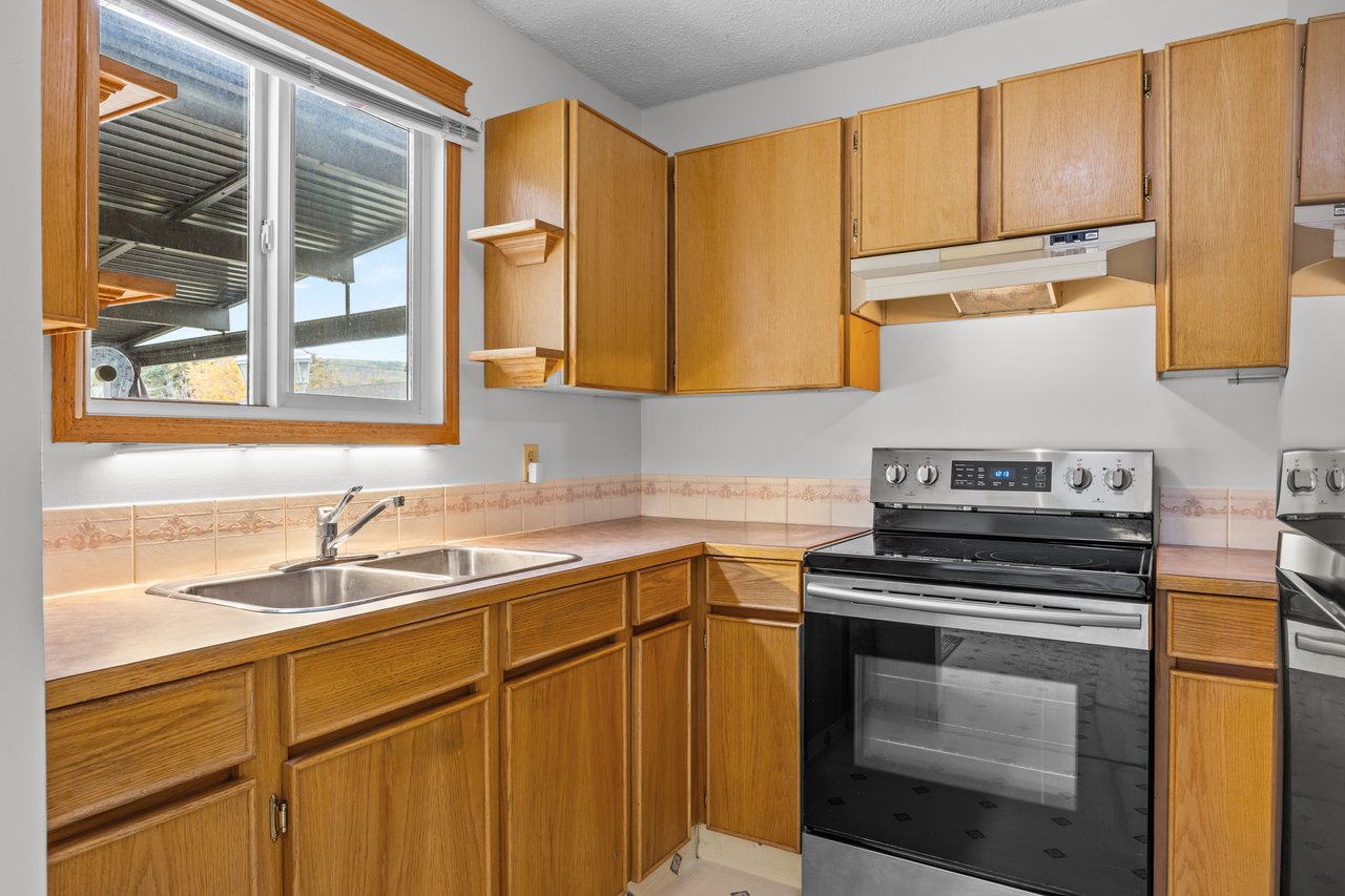 Kitchen with honey-toned wood cabinets, double sink beneath a window, and black-and-stainless electric range.