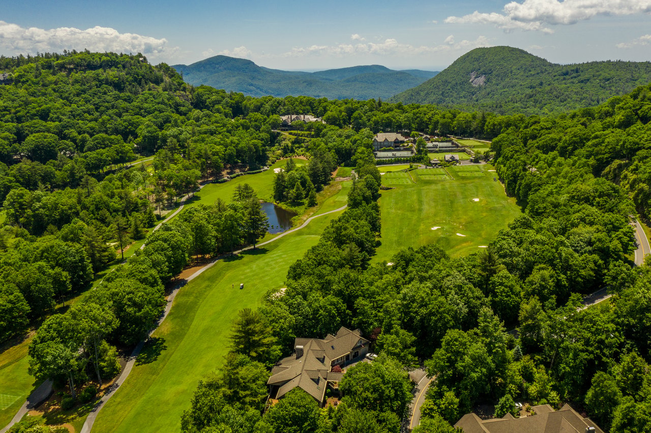 Aerial view of Cullasaja Club golf fairways, a pond, and homes surrounded by forest and mountains in Highlands, NC