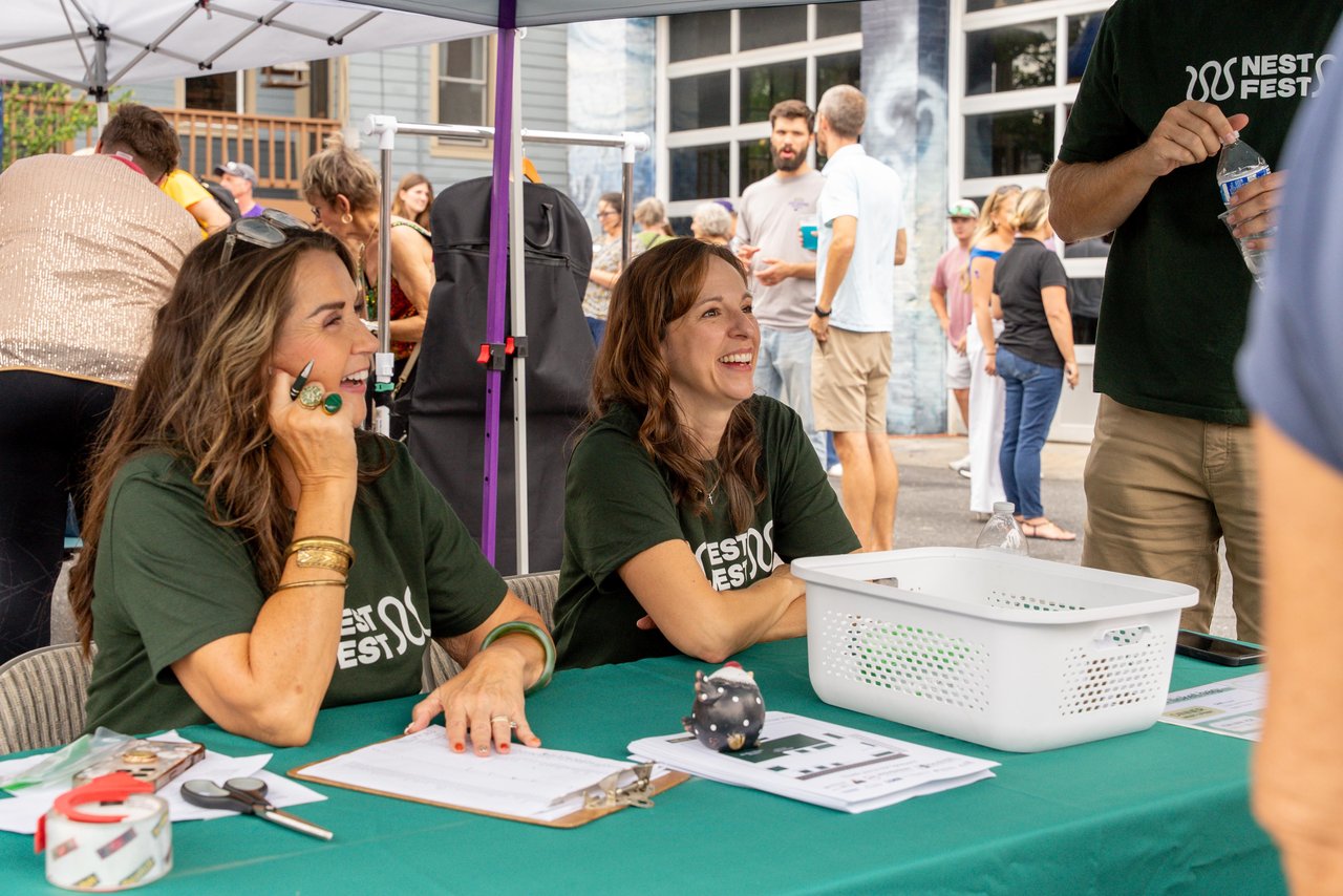 Nest Fest staff members chat with visitors at an outdoor event booth.