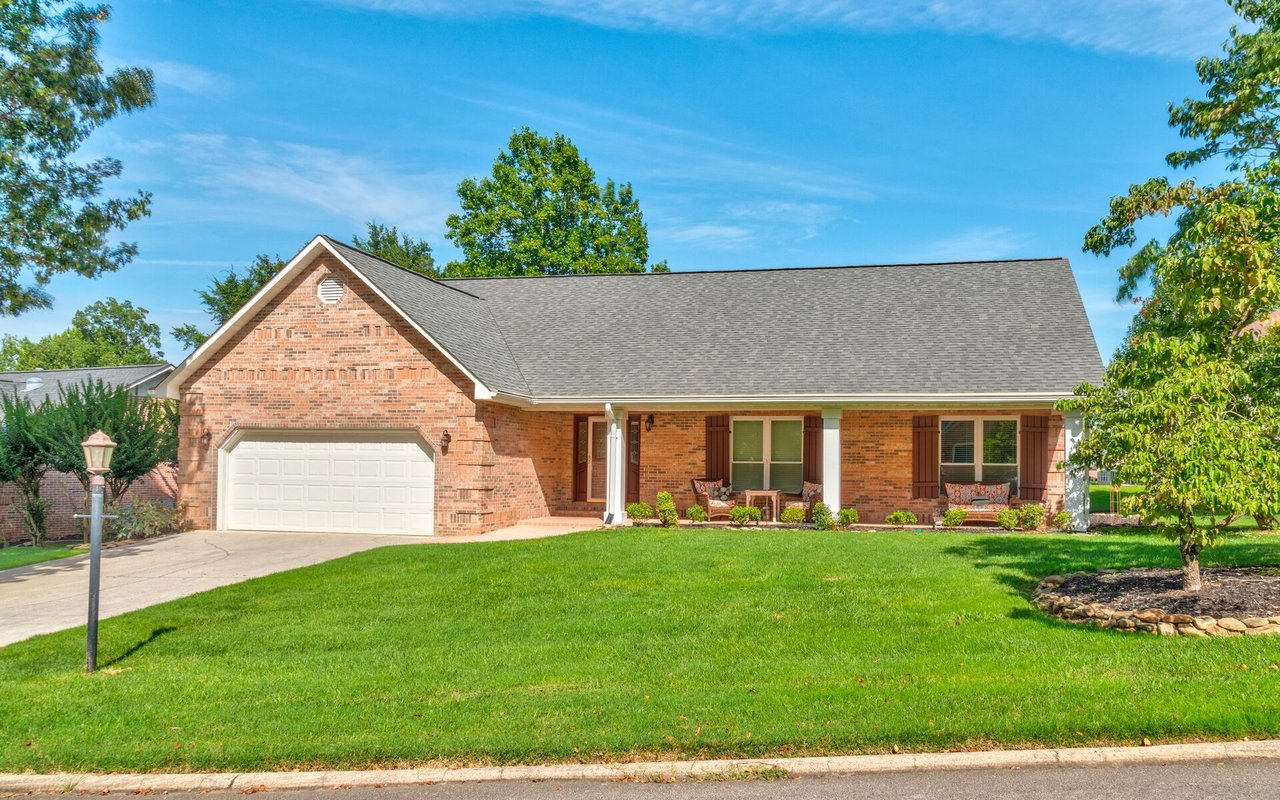 Brick ranch-style home with an attached garage, covered front porch, and broad green lawn.