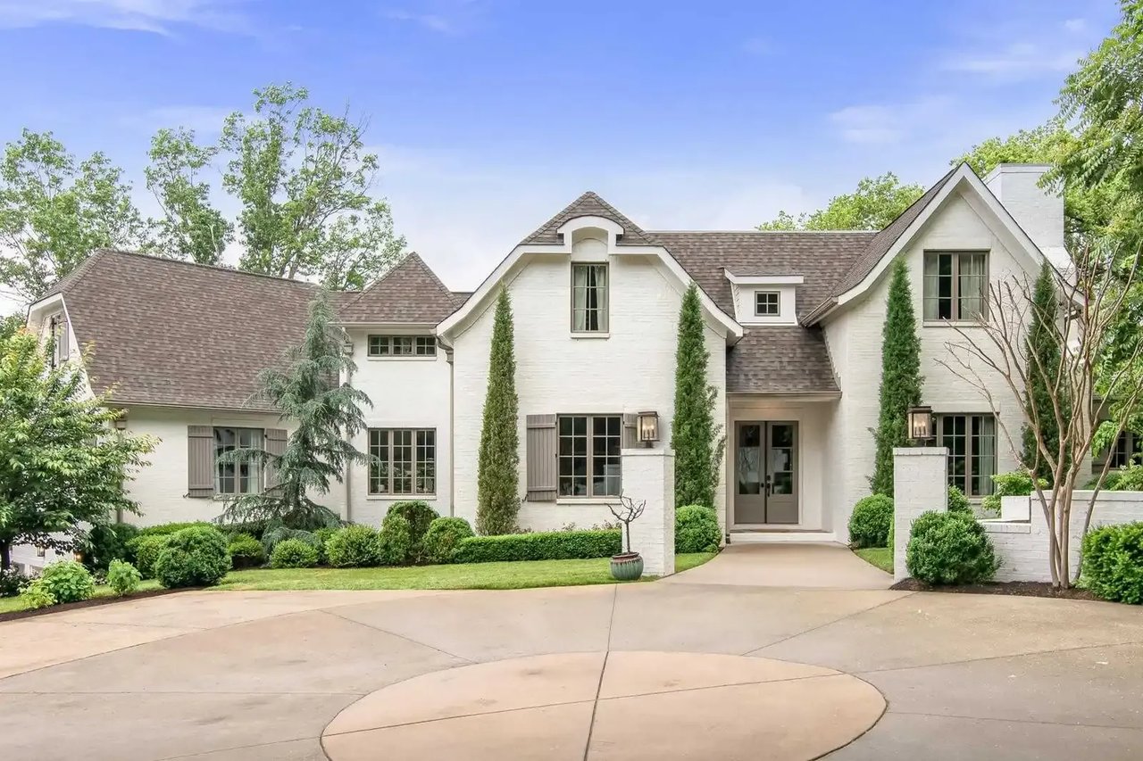 White-brick house with steep gables, landscaped entrance, and broad curved driveway.