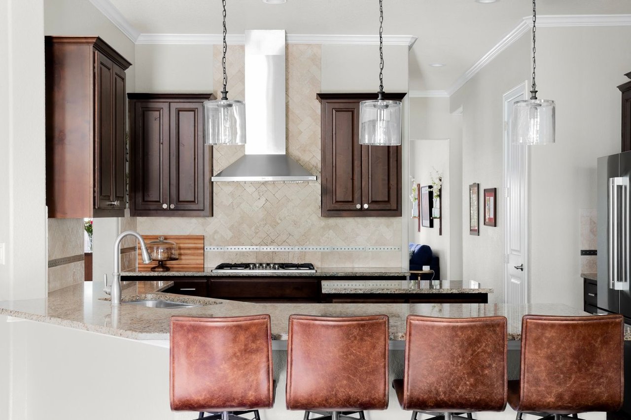 Kitchen with dark wood cabinets, a stone island, and four leather bar stools.