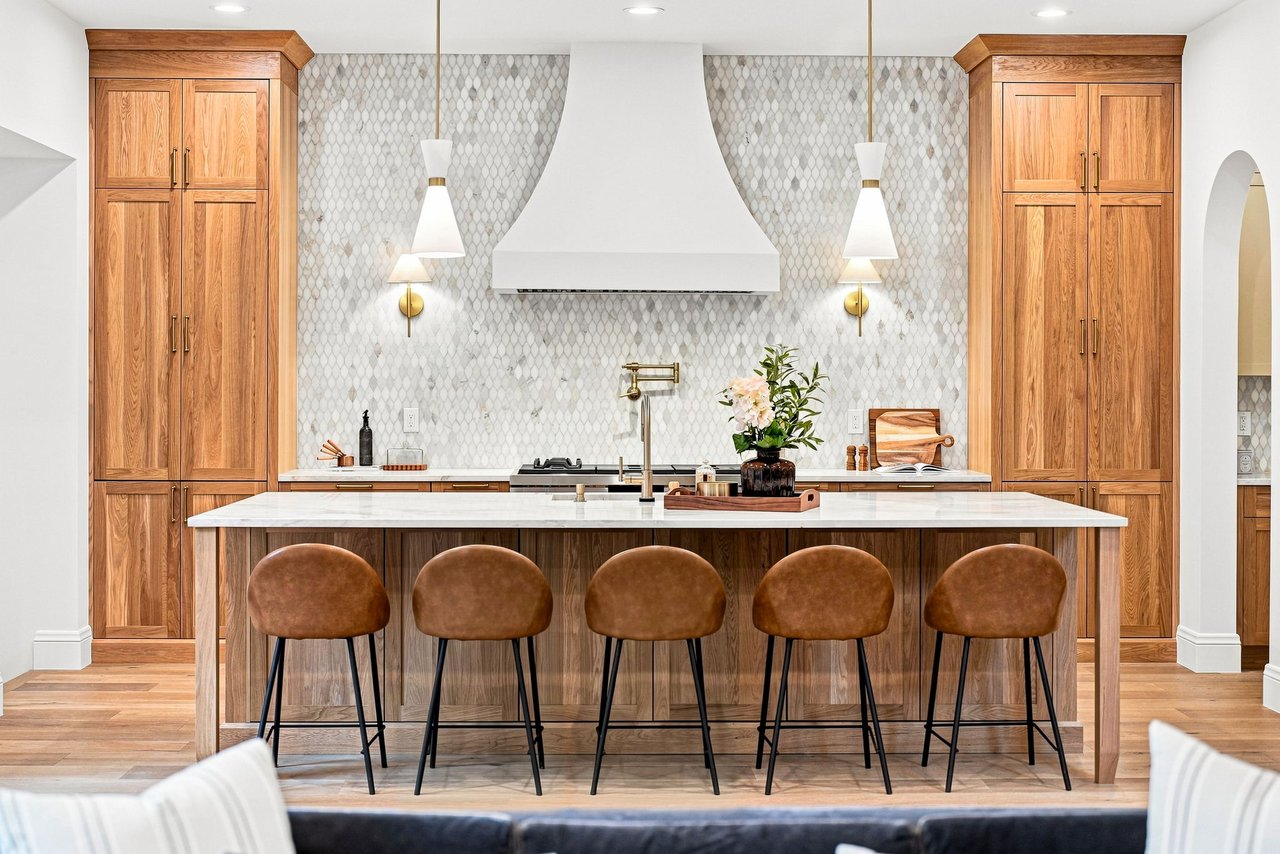 Kitchen with a wood-paneled island, five brown stools, tall oak cabinets, and patterned tile backsplash.