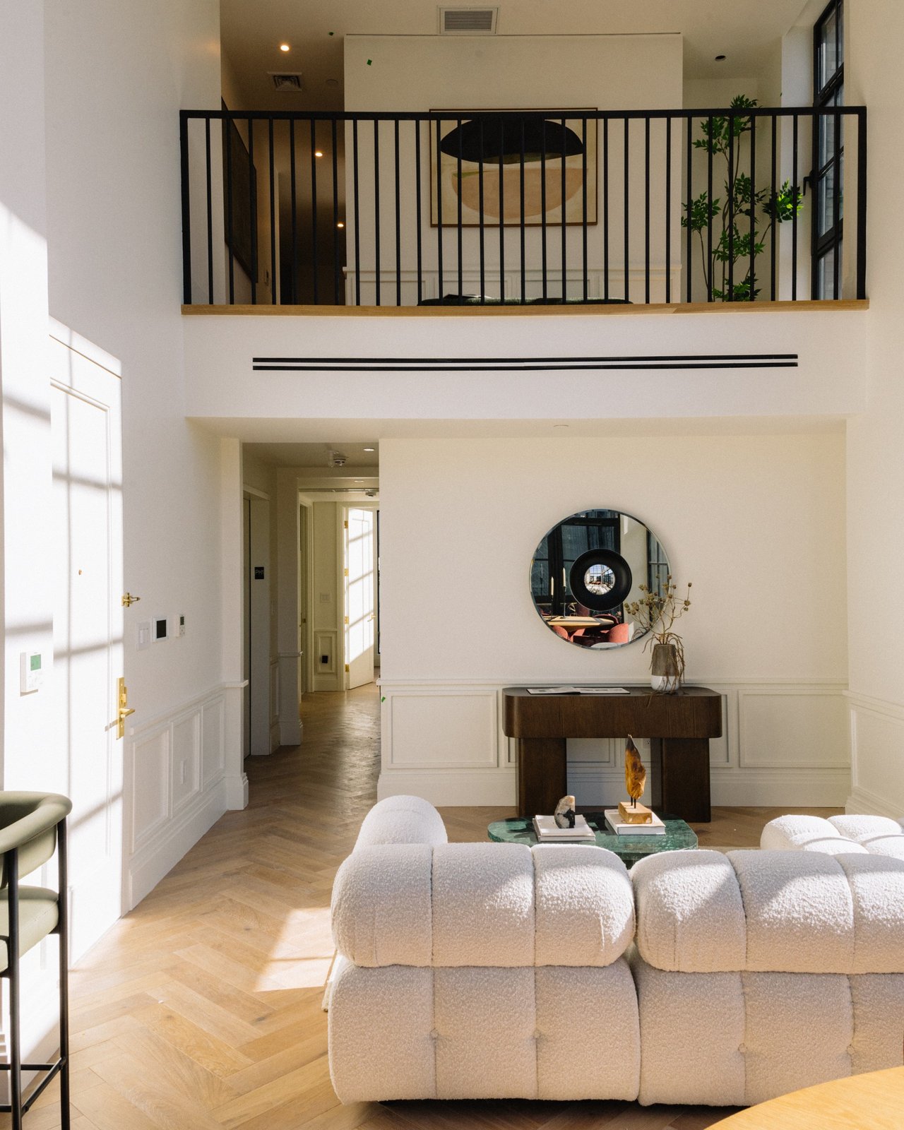 Double-height living room with a black-railed mezzanine and sculptural white seating.