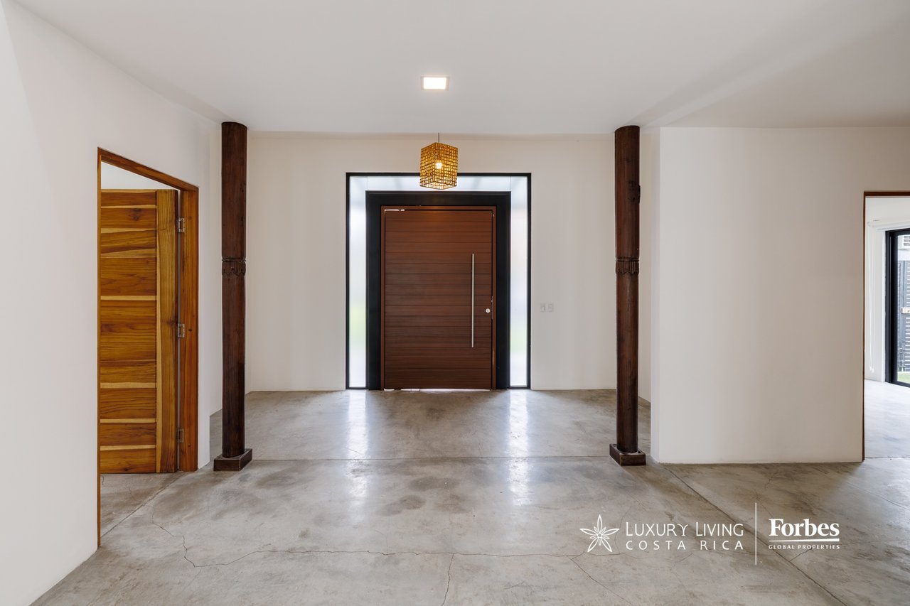 Entry hall with a wide wooden front door, dark timber columns, and a polished concrete floor.