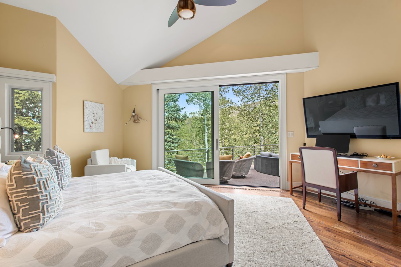 Bedroom with vaulted ceiling, sliding glass doors, and a tree-lined balcony view.