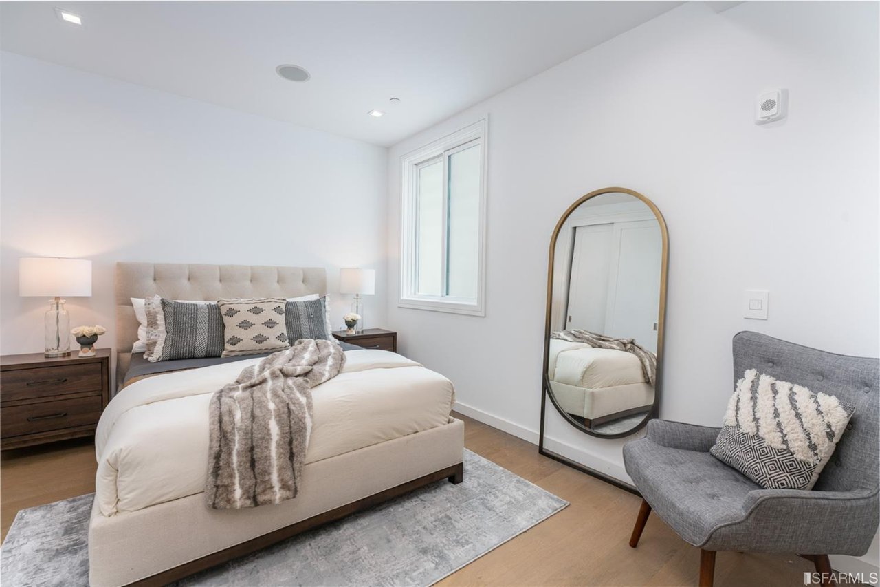 Bright bedroom with upholstered bed, armchair, and large mirror