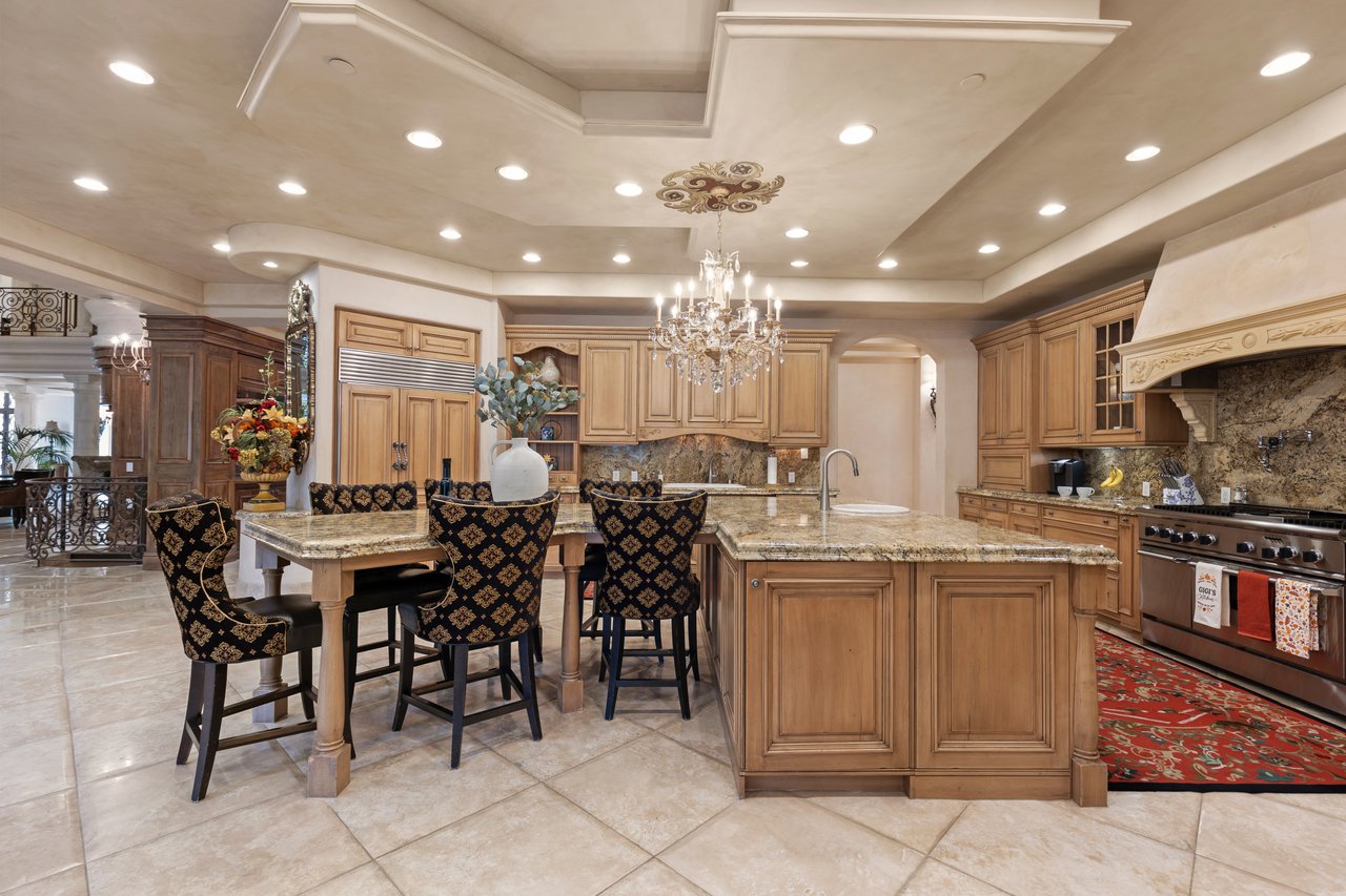 Expansive kitchen with a granite island, ornate chandelier, warm wood cabinetry, and patterned dining chairs.