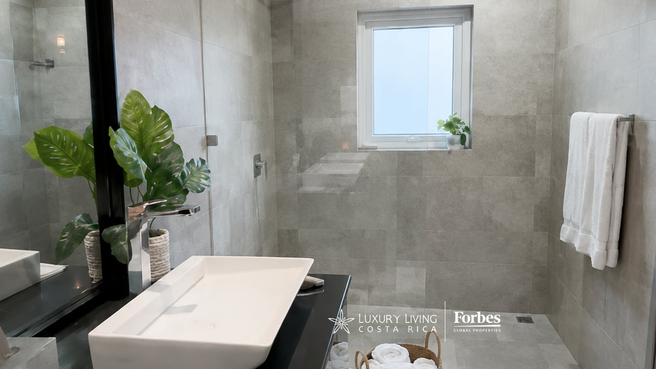 Bathroom with gray stone tile, glass shower, and a white vessel sink on a dark vanity.