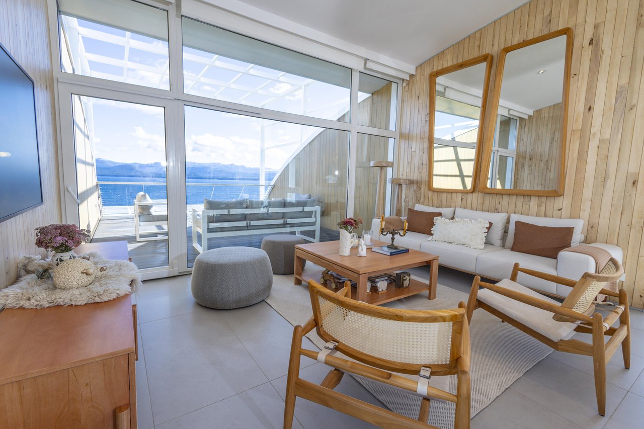 Furnished living room with wood-paneled walls and a terrace overlooking water and mountains.