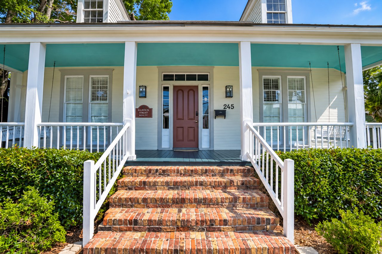 Front of a white-sided building with a teal porch roof and broad brick steps.