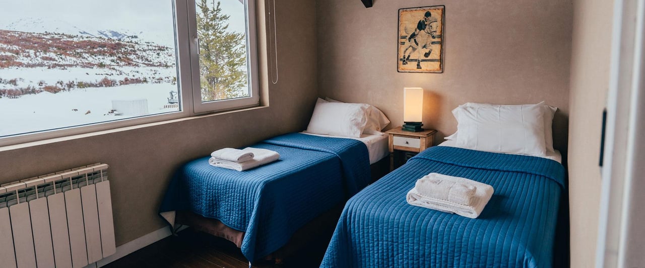 Bedroom with two blue-covered single beds and a window overlooking a snowy mountain
