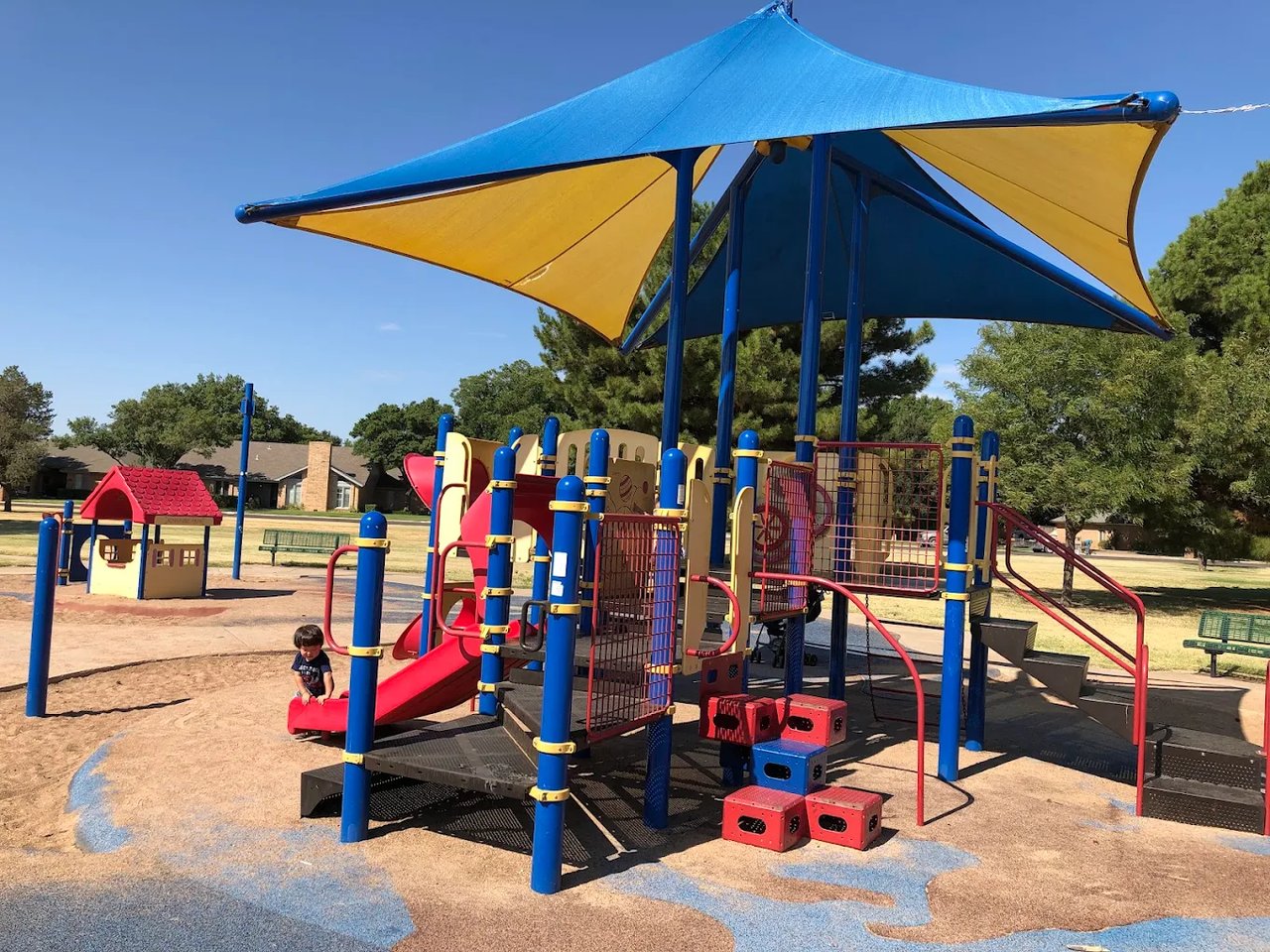 Playground with colorful climbing structures and slides beneath a blue-and-yellow shade canopy.