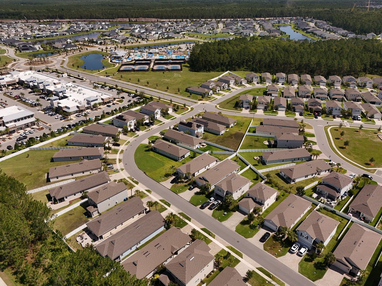 Aerial view of a residential community with curving streets, recreation pools, and surrounding woodland.